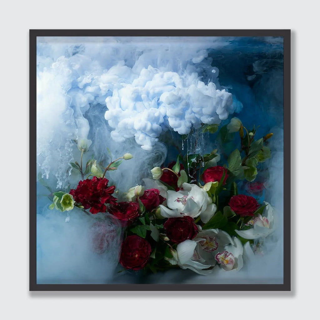 A framed square art print featuring a still life of red and white flowers with green leaves set against a smoky blue and white background, displayed on a light gray wall.