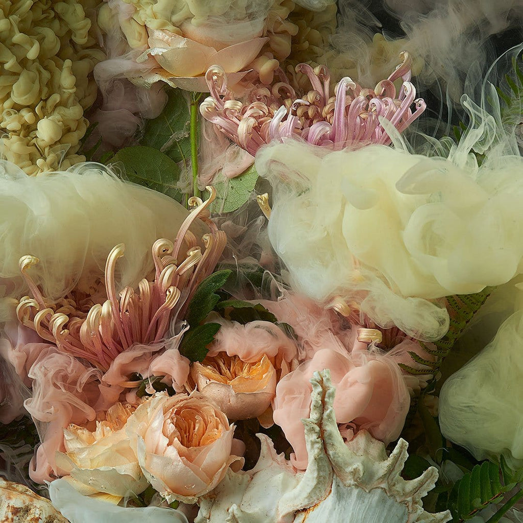 A close-up arrangement of soft pastel flowers and feathery botanical elements, including blush pink roses, pale peach blossoms, cream feathery petals, and textured pale yellow flowers with metallic gold centers.