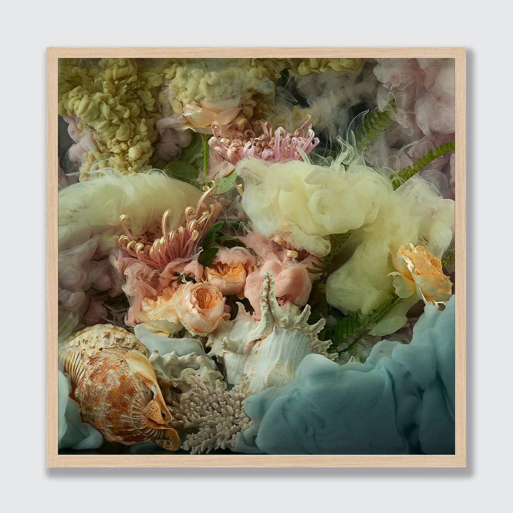 A framed square art print featuring a surreal still life of pastel flowers, seashells, coral, and flowing blue-green and cream textures, set against a light gray background.