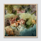 A framed square art print featuring a surreal still life of pastel flowers, seashells, coral, and flowing blue-green and cream textures, set against a light gray background.