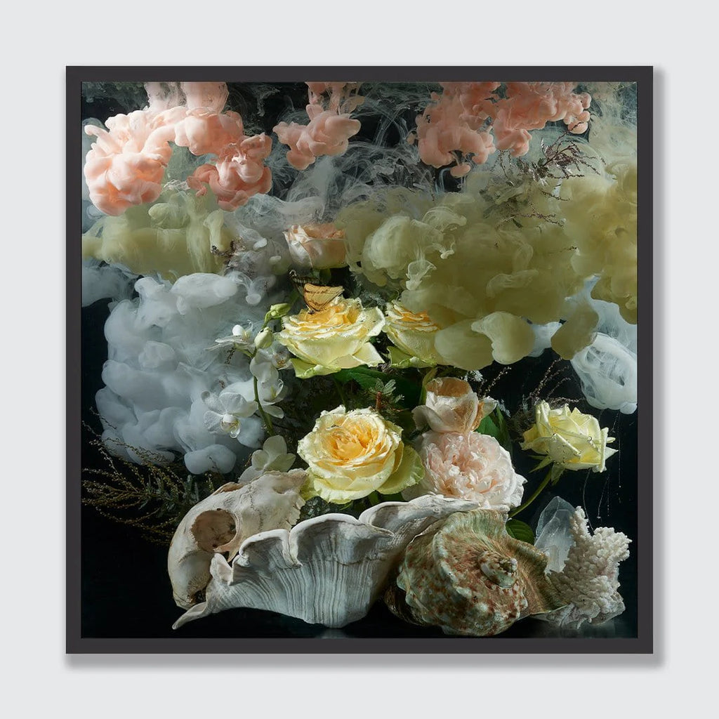 A framed square art print featuring a still life composition of soft peach, cream, and yellow flowers with white and beige seashells on a dark background, shown against a light gray wall.