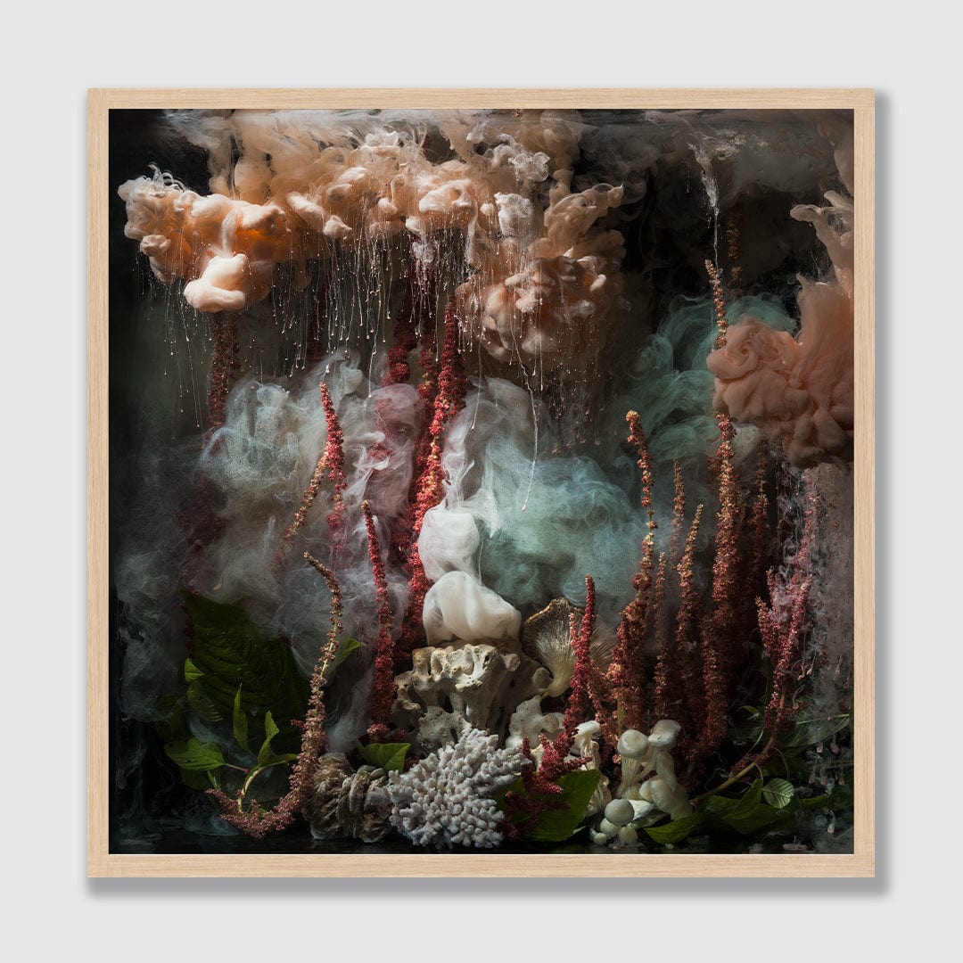 A framed square art print featuring an abstract underwater-like scene with flowing smoky clouds in beige, white, and pale green, red-brown vertical spires, dark foliage, and coral-like textures, set in a light natural wood frame against a light gray background.