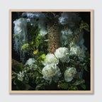A framed square art print featuring a moody floral still life with white flowers, green leaves, and textured dark foliage against a black background, set in a light natural wood frame.