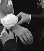 Black and white close-up of a person wearing a white rose wrist corsage while another person adjusts it.
